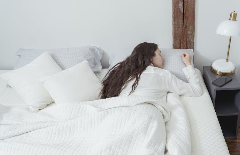 A woman with long hair peacefully sleeping in a cozy, well-lit bedroom, embodying tranquility.